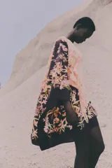 Vestido túnica con estampado floral en tonos rosados y negros, de tejido arrugado, silueta oversized, mangas largas con gran volumen y cuello redondo con abertura de cerradura y botón oculto en la nuca. Largo hasta la rodilla.