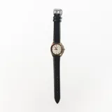 Reloj de pulsera con caja dorada de forma octogonal y esfera blanca con números arábigos. Correa de cuero negra.