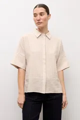 Camisa de manga corta con diseño a rayas en tonos beige y blanco, cuello camisero y cierre frontal con botones ocultos.