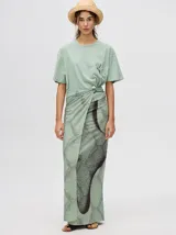 Pareo largo de viscosa en color verde menta, con diseño estampado que presenta gráficos abstractos y una figura central destacada en negro. Es una prenda liviana y fresca, ideal para usar sobre el traje de baño o como falda envolvente.