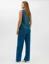 Conjunto de tres piezas compuesto por musculosa, cardigan y pantalón. La musculosa y el cardigan presentan un diseño plisado con hilos metalizados en tonos verdes y azules, creando un efecto tornasolado. El cardigan es de frente abierto con mangas 3/4 y corte fluido. El pantalón es de seda fría en color azul petróleo, con cintura elastizada. Incluye un collar removible.