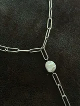 Corbatín con cadena de acero quirúrgico color plateado y perlas de río. Se puede usar ajustado al cuello o más suelto. Se cierra con ganchito para regular el largo.