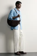 Bolso de hombro de diseño semicircular, confeccionado en piel con acabado serraje de color marrón. Cuenta con una sola asa de hombro y cierre principal con cremallera.