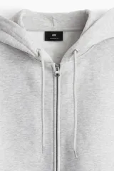 Campera con capucha y cierre frontal de H&M, color gris melange, con hombros caídos, bolsillos tipo canguro y ajuste oversized.
