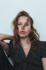 Camisa negra con estampado de lunares blancos, cuello redondo con escote en pico, mangas cortas abullonadas y detalle de volantes frontales. Cierre frontal con botones.