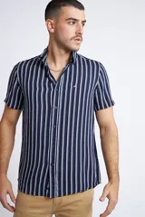 Camisa de manga corta con diseño a rayas verticales en color azul marino y blanco. Presenta cuello clásico, cartera abotonada frontal y logo bordado en el pecho. Posee un corte slim fit.
