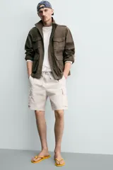 Bermuda cargo color negro de corte relaxed fit, confeccionada en tejido de algodón con elasticidad y efecto lavado. Cuenta con cintura elástica ajustable con cordón, bolsillos frontales y bolsillos laterales tipo cargo con solapa en las perneras.