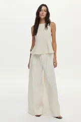 Top de lino color beige con cuello bote y diseño con peplum, sin mangas y con cierre invisible en la espalda.