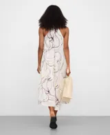 Vestido midi color crudo con estampado de flores abstractas en tonos morados y oliva, corte evasé, escote en V y cuello halter anudado en la espalda.