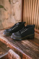 Borcego negro de cuero con cordones, suela track y detalle de costuras amarillas.