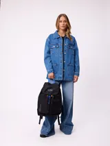 Mochila urbana marca Rusty de color negro, con múltiples compartimentos frontales, bolsillo de red lateral y detalles en azul y amarillo. Presenta el logo de la marca en la solapa superior y el texto 'Rusty Worldwide' en el frente.