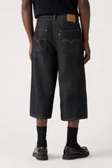 Pantalón capri de denim negro con corte amplio, tiro alto y cinturón de tela con hebilla metálica.