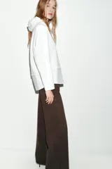 Camisa blanca de manga larga con un top de sudadera gris claro superpuesto, que incluye capucha ajustable con cordones. El bajo de la camisa tiene aberturas laterales.