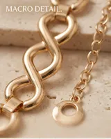 Cinto de metal dorado con eslabones entrelazados en forma de ocho y una cadena colgante fina con un dije circular en el extremo.