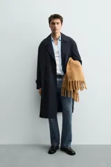 Trench de corte relajado confeccionado en tejido con viscosa, de color azul marino. Presenta cuello con solapas de muesca, cierre frontal de botonadura cruzada, mangas largas con puños ajustables mediante trabillas y bolsillos de vivo en la cadera. Incluye una abertura central en la espalda.