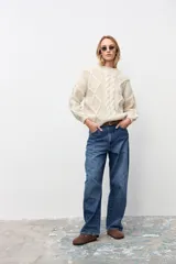 Sweater de tejido de punto grueso color crudo, con diseño de trenzas frontales, cuello redondo y mangas largas con puños ajustados.