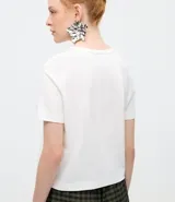 Remera de algodón color blanco, de corte clásico con cuello redondo y manga corta. Presenta un delicado bordado de tres pequeños íconos florales en el centro del pecho.