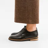 Zapato mocasín de cuero vacuno color negro, con cordones y punta redonda. Tiene taco de madera foliado en cuero de 2,5 cm y entre suela de goma de 1 cm.