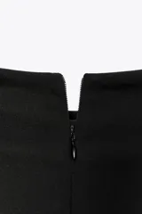 Vestido midi de color negro, con cuello subido y diseño sin mangas. Presenta un detalle de drapeado lateral en la parte delantera y cierre de cremallera oculta en la espalda.