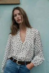 Blusa de escote en pico con volantes frontales, manga larga con puños elásticos y cierre frontal con botones.