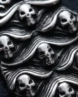 Dije de acero color plateado con diseño texturizado que incluye siete calaveras y detalles de ondas.