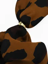 Pañuelo de seda con estampado geométrico en blanco, negro y gris, que incluye un anillo metálico dorado para sujetarlo.