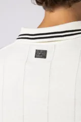 Remera tipo chomba de tejido de punto color blanco, con cuello polo y diseño de rayas verticales sutiles. Presenta estampado gráfico frontal con texto y logo, además de detalles de rayas negras en los hombros.