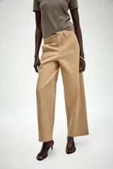 Pantalón de sarga en color beige, con tiro medio, cintura con trabillas y pernera recta. Presenta bolsillos de vivo en el delantero, cierre frontal con cremallera y botón metálico.