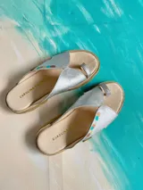 Sandalias de cuero plateado metalizado, con diseño de tira al dedo y detalles pintados a mano en el empeine. Poseen suela plana con borde texturizado de yute.