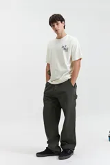 Remera de manga corta color crema, con escote redondo y ajuste regular. Presenta un estampado en la espalda con flores azules y texto en negro que dice "FEEL GOOD" en vertical, "ALL DAY EVERY DAY THE GOOD VIBES CREW mistral" y "ALWAYS IN GOOD COMPANY SINCE 1976".