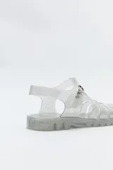 Sandalias jelly color gris translúcido, con diseño entrecruzado y hebilla lateral ajustable.