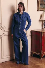Mono de denim azul con cierre frontal de botones metálicos, cuello camisero, mangas largas y corte de pierna ancha. Incluye bolsillos delanteros y traseros.