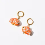 Par de aros colgantes con argolla dorada y dije de cerámica naranja con forma de pez y detalles en azul.