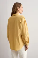 Camisa amarilla de manga larga con detalles bordados y calados en los hombros, pecho y mangas, corte clásico con cuello camisero y cierre frontal de botones.
