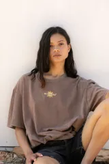 Remera oversize de algodón con efecto lavado, color negro, de manga corta y cuello redondo. Presenta una estampa gráfica en la espalda con motivos solares y tipografía en tonos naranja y amarillo.