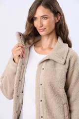 Campera de sherpa color beige, con cuello camisero, cierre frontal con botones a presión y detalles de ribete en la solapa y puños.