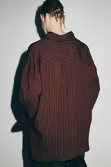 Camisa de corte oversize confeccionada en mezcla de viscosa, con diseño de rayas verticales, cuello solapa, manga larga con puños, bolsillo de plastrón en el pecho y cierre frontal con botones.
