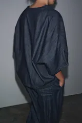 Camisa de tejido tipo denim azul oscuro, con escote pico, manga corta ancha y dos bolsillos de parche frontales. Cierre frontal con botones.