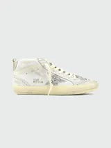 Championes de caña media Golden Goose modelo Mid Star, color blanco con efecto desgastado. Presentan una estrella lateral con glitter plateado, detalles de perforaciones tipo brogue y suela con acabado envejecido.