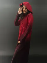 Tapado rojo con capucha, confeccionado en lana merino teñida con técnica tie-dye. Tiene corte recto, largo, bolsillos laterales y cierre cruzado con broches a presión ocultos.