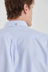 Camisa de vestir blanca de manga larga, con cuello abotonado, bolsillo frontal y botones en tono madera.