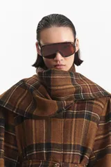 Abrigo largo tipo trench con estampado a cuadros en tonos marrones. Presenta un cuello que simula una bufanda integrada, cierre mediante lazo ajustable en la cintura y mangas largas. Confeccionado en una mezcla de lana y poliéster con forro interior.