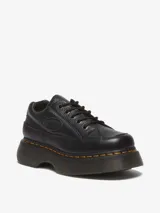 Zapatos Dr. Martens Buzz 5i de cuero negro con textura granulada, suela de plataforma gruesa con pespuntes amarillos, cierre de cordones y logo de la marca en relieve en el lateral.