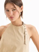Top Lucille de silueta evasé, calce holgado y corte cropped, confeccionado en poplín Milano de algodón Pima. Cuenta con escote halter de sisa profunda, bretel regulable con ojalillos de níquel que envuelve el cuello, pinzas de entalle y espalda abierta.