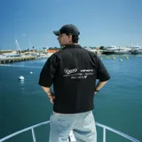 Camisa negra de corte oversize, manga corta y cuello tipo bowling. Presenta botones frontales y estampado con el logo de la marca en el pecho.