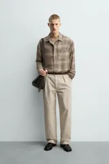 Camisa relaxed fit de manga larga con cuello solapa, confeccionada en tejido con mezcla de viscosa. Presenta un bolsillo plastrón en el pecho, bajo con aberturas laterales y cierre frontal de botonadura. El diseño es a cuadros en tonos beige y marrón.