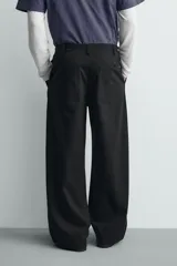 Pantalón wide fit de algodón con efecto lavado, corte recto y holgado. Presenta un cierre frontal cruzado con botones y un alamar metálico distintivo, además de bolsillos frontales y traseros de plastrón.
