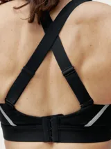 Top deportivo color beige con tirantes regulables cruzados en la espalda y cierre ajustable. Presenta una banda reflectante en el frente y copas extraíbles.