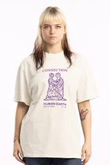 Remera de corte holgado en color beige, con cuello redondo y mangas cortas. Presenta un estampado gráfico central en color violeta que representa dos figuras humanas entrelazadas con el texto 'CONNECTION HUMAN/EARTH'.