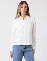 Camisa de crepe color beige con cuello clásico, cierre frontal con botones y dos bolsillos aplicados en el pecho.